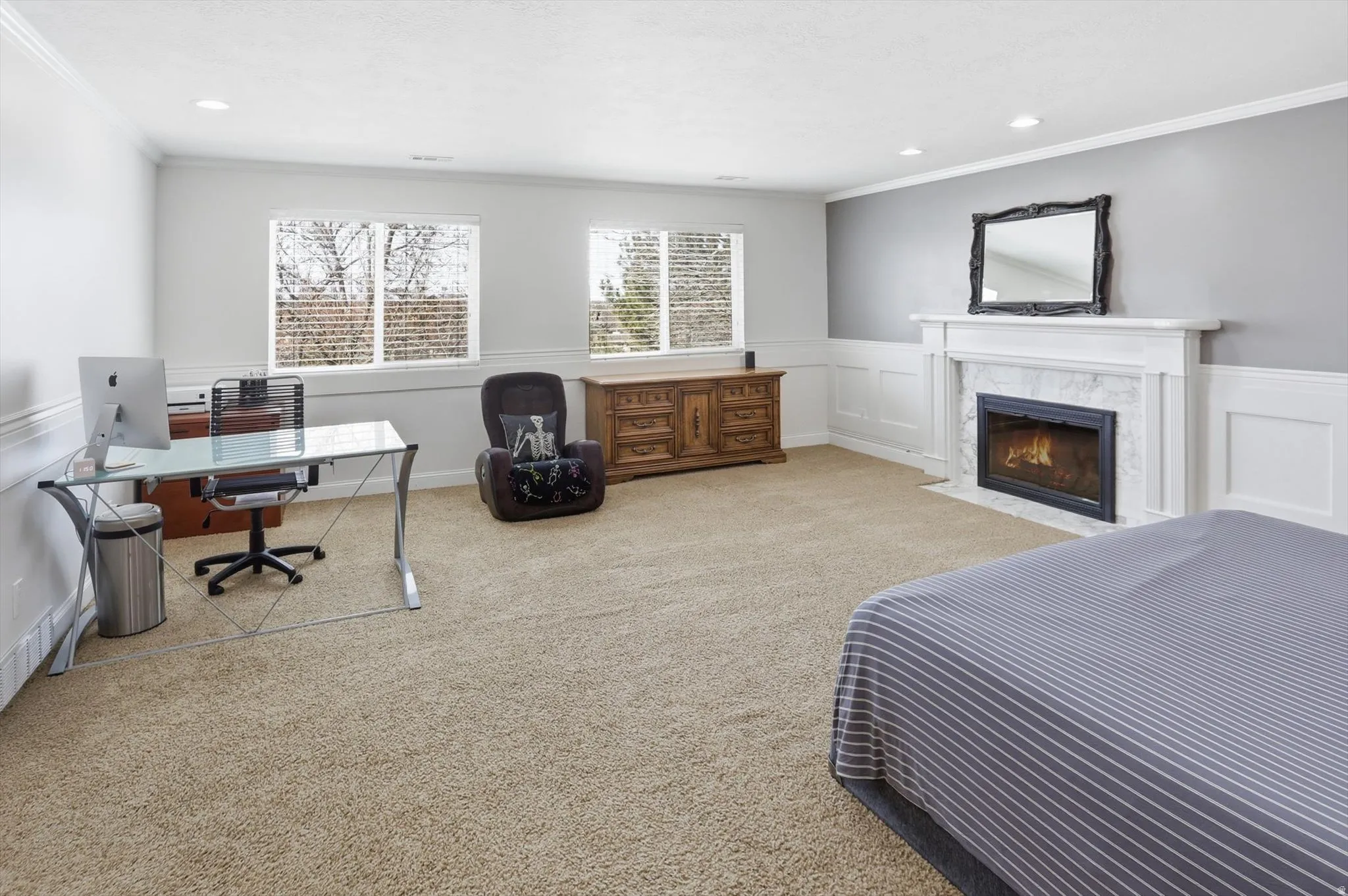 Carpeted bedroom featuring a decorative wall, wainscoting, a desk, crown molding, and a fireplace