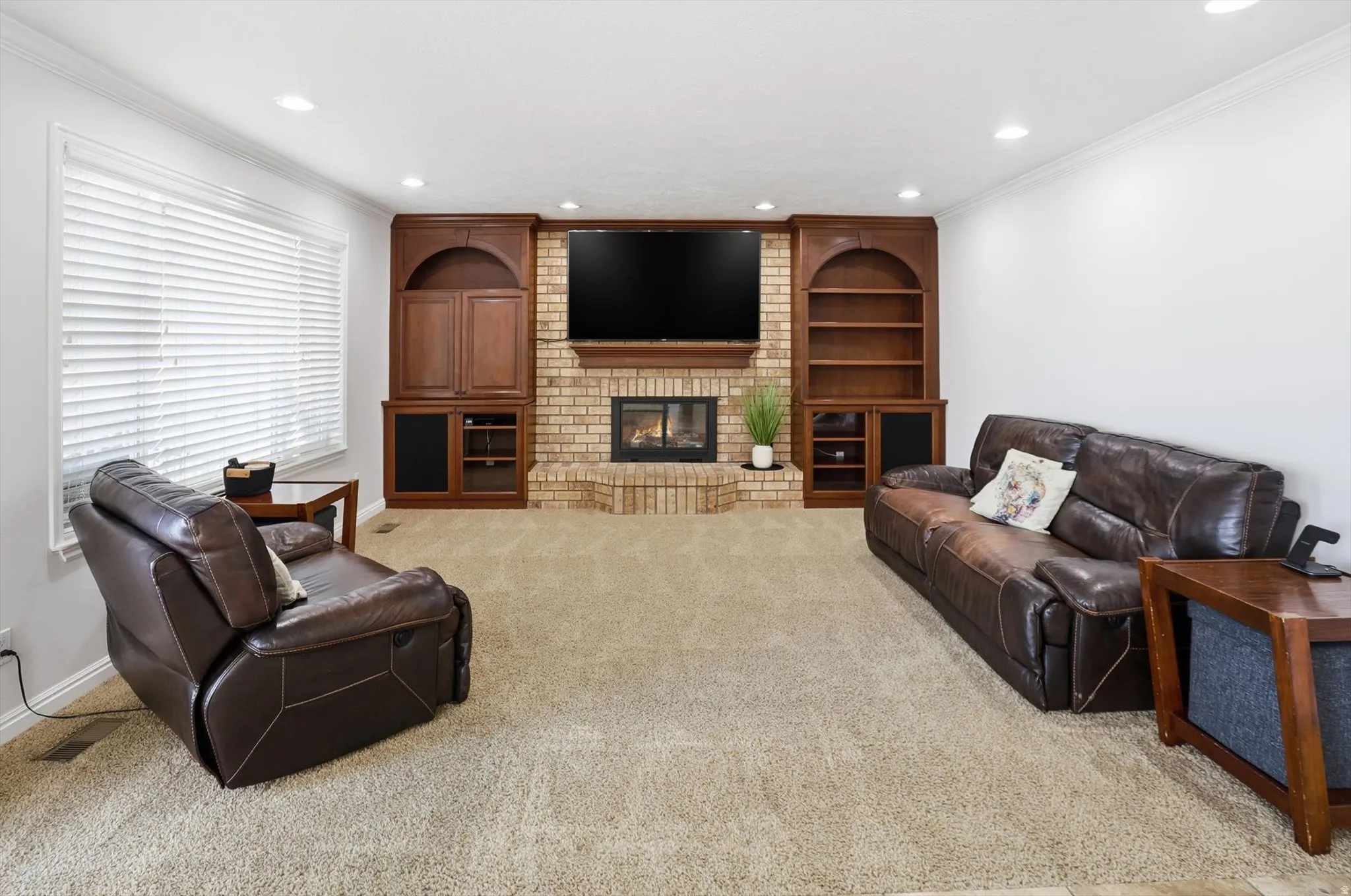 Living room featuring crown molding, recessed lighting, a brick fireplace, built in shelves, and light carpet