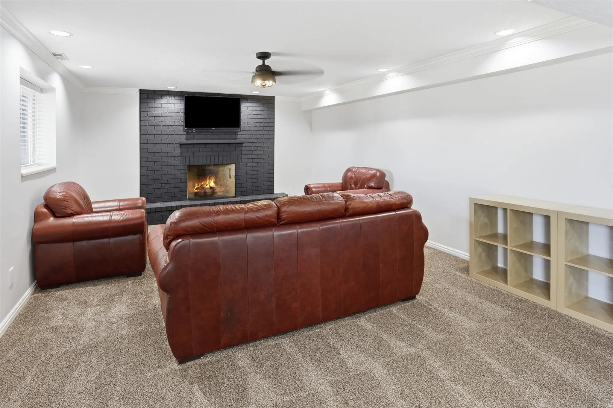 Carpeted living room with crown molding, a ceiling fan, a brick fireplace, and recessed lighting