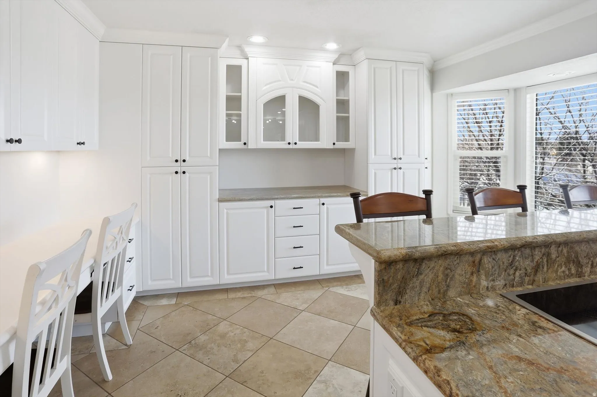 Kitchen with glass insert cabinets, white cabinets, dark stone counters, ornamental molding, and recessed lighting