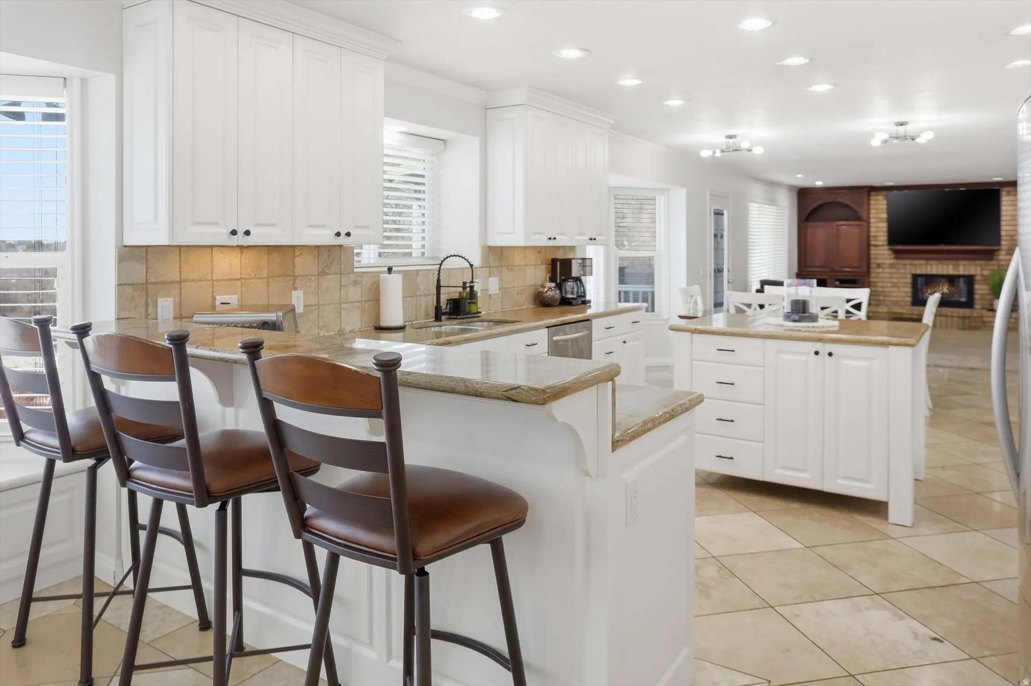 Kitchen featuring white cabinets, a kitchen breakfast bar, a fireplace, a peninsula, and recessed lighting