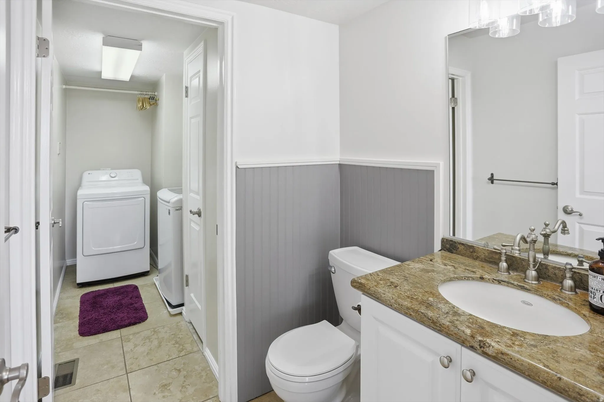 Bathroom featuring vanity, washer and dryer, a wainscoted wall, and light tile patterned flooring