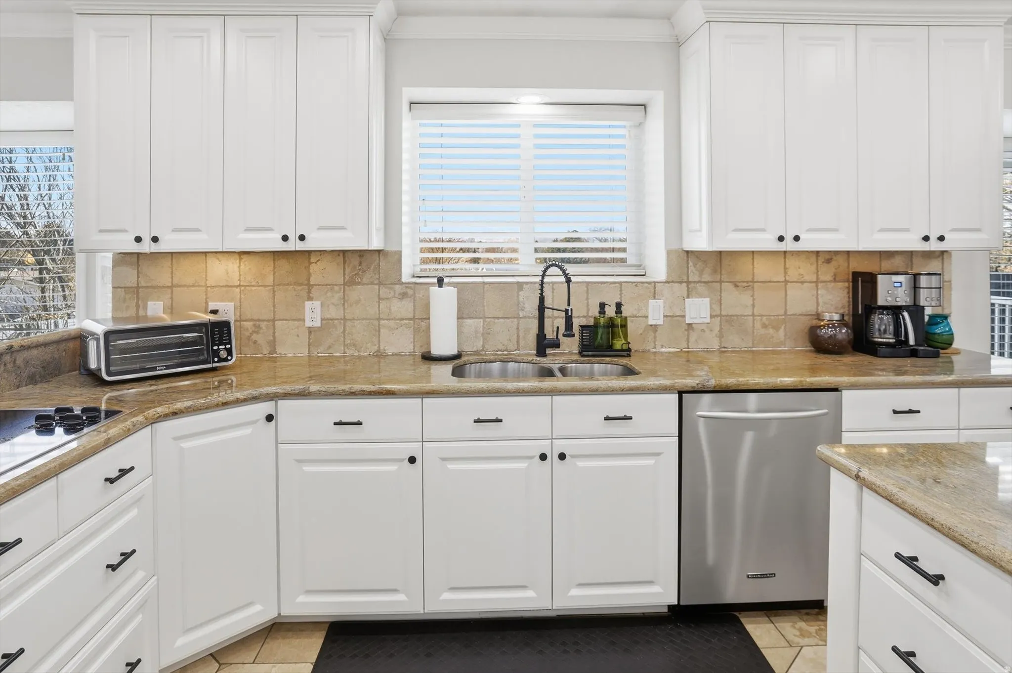 Kitchen with white cabinets, stainless steel dishwasher, light stone counters, tasteful backsplash, and crown molding