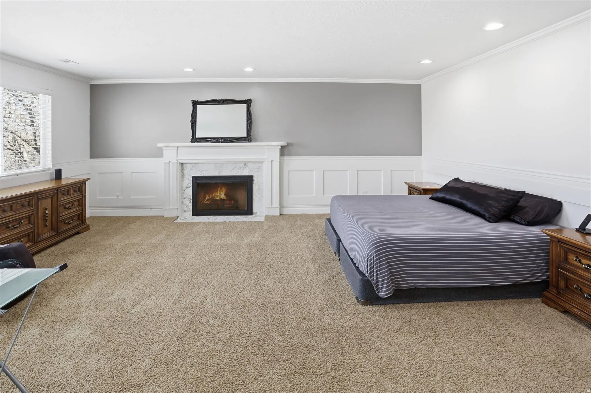 Bedroom with wainscoting, a decorative wall, light carpet, crown molding, and a premium fireplace