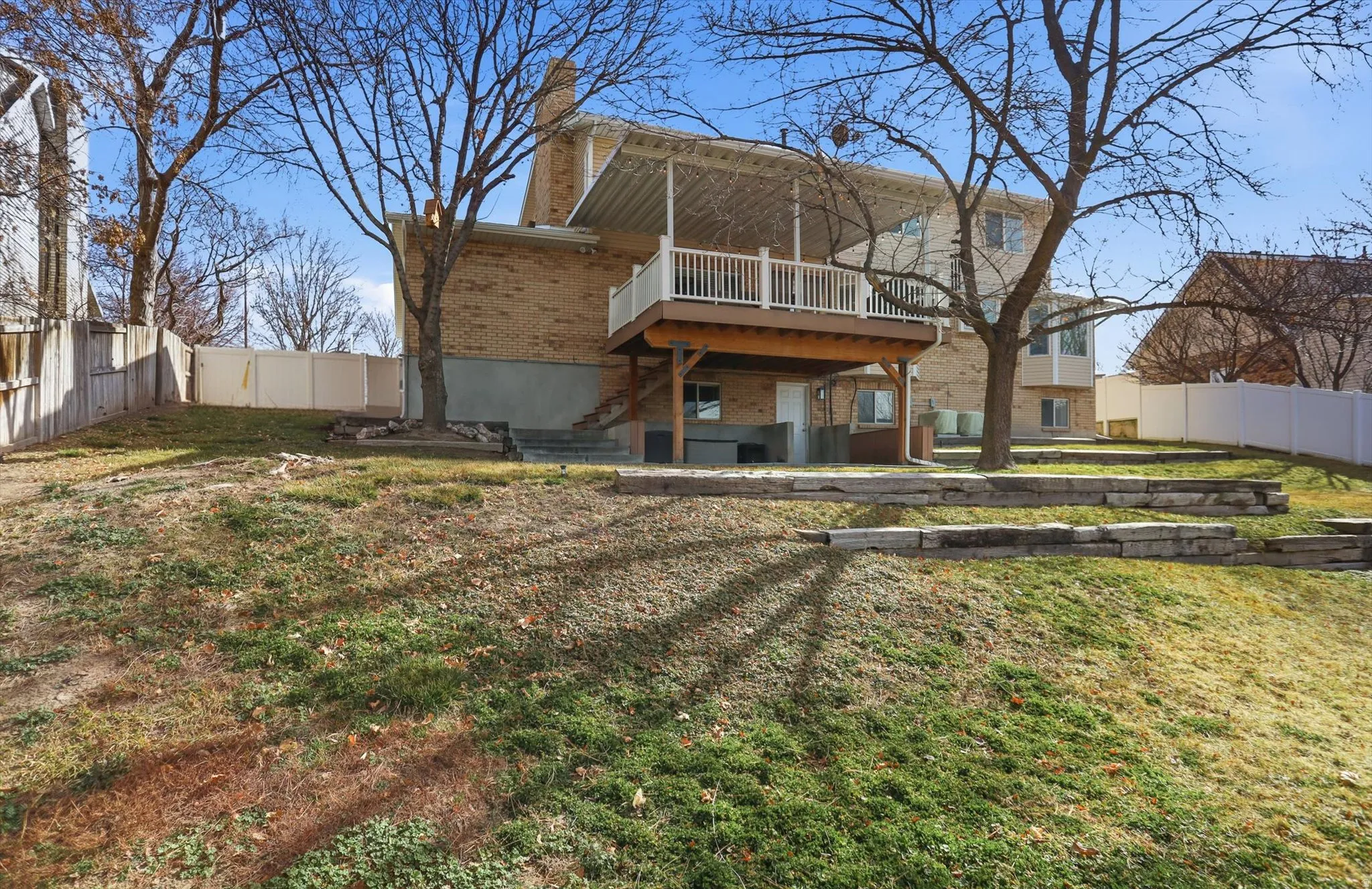 Rear view of property featuring a fenced backyard, brick siding, a chimney, a wooden deck, and a patio area