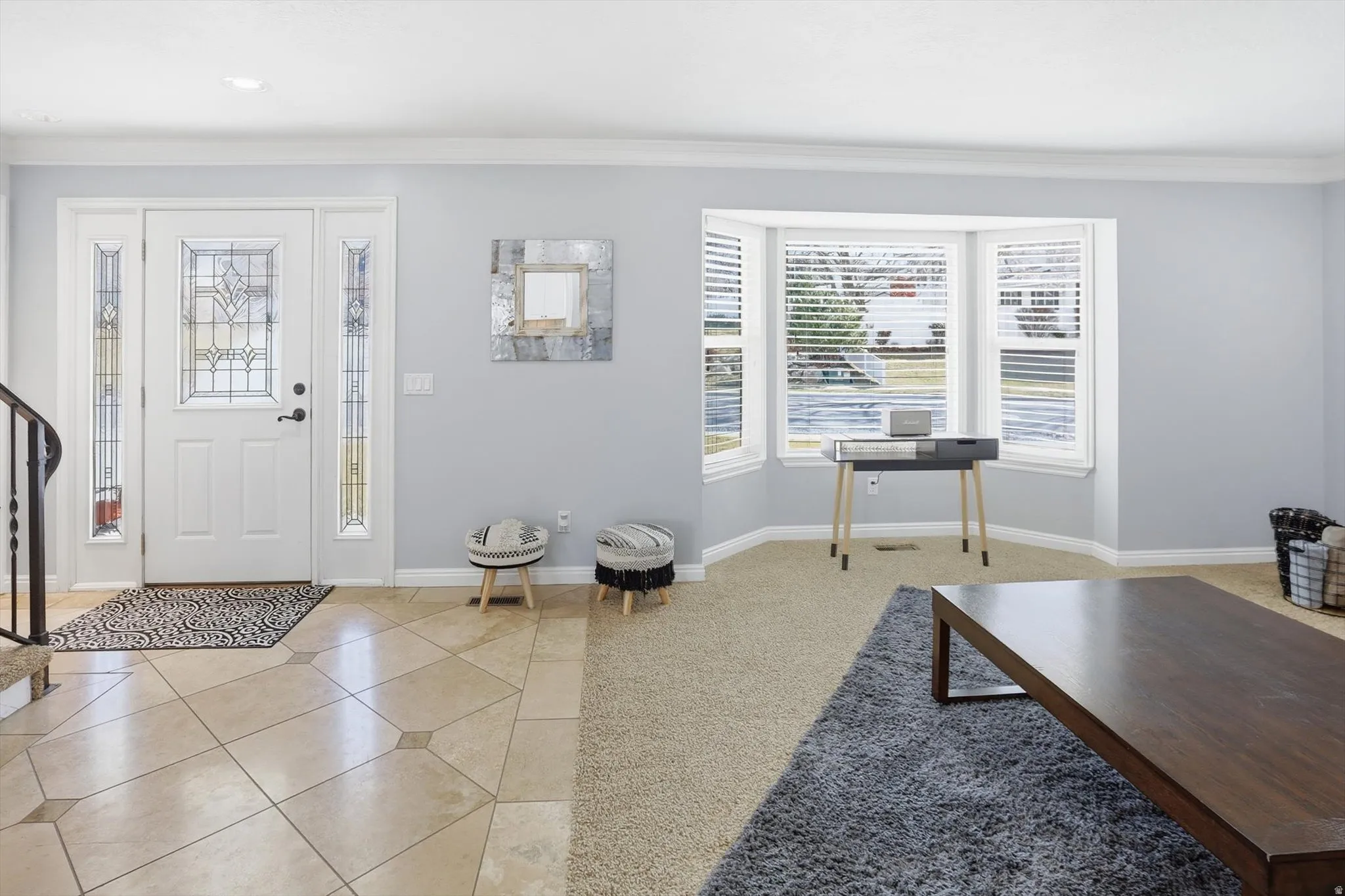 Entryway with light tile patterned floors, light carpet, and ornamental molding