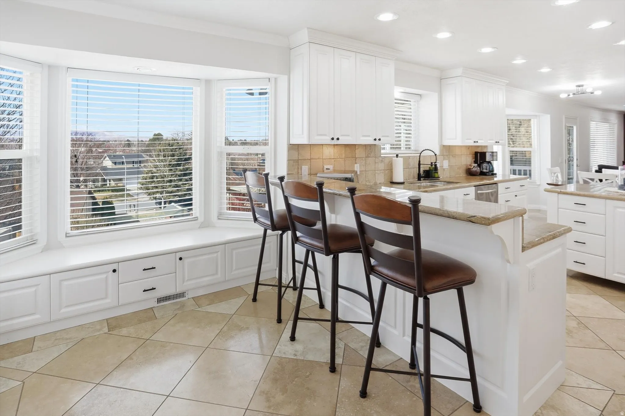Kitchen featuring white cabinets, crown molding, backsplash, a kitchen bar, and recessed lighting
