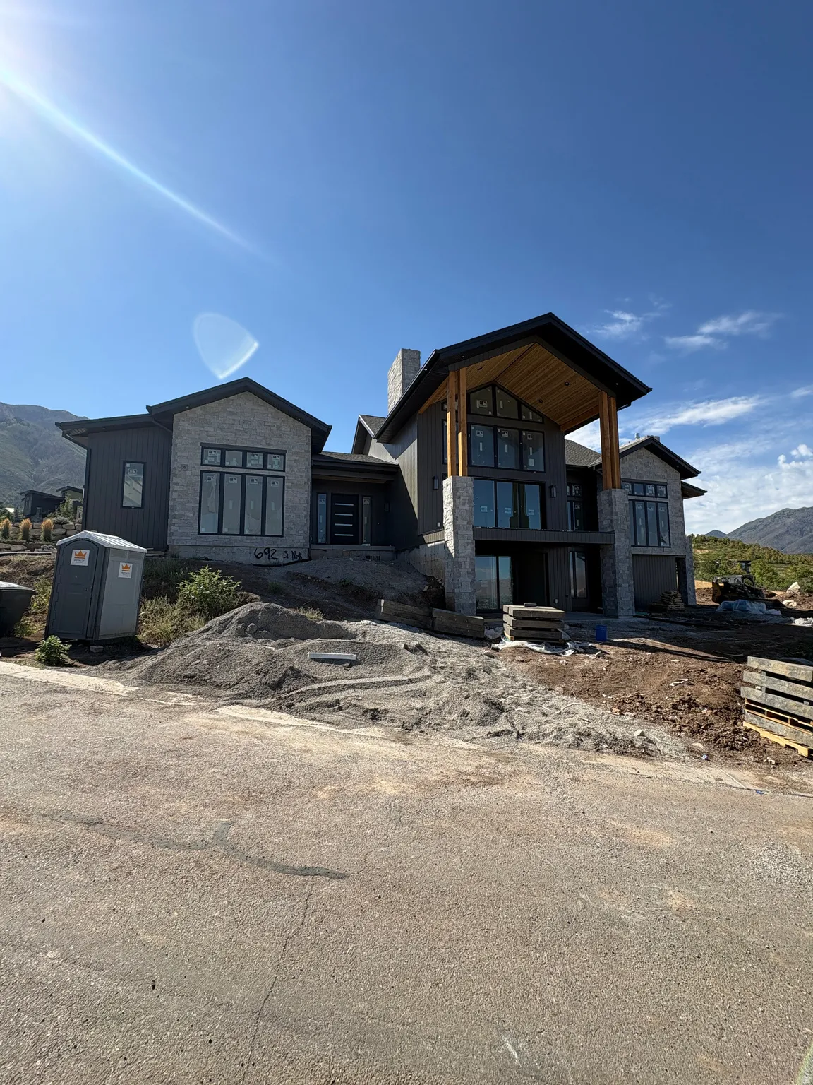 Modern architectural design featuring stone and dark siding, extensive fenestration, and a prominent covered entryway with exposed wood beams