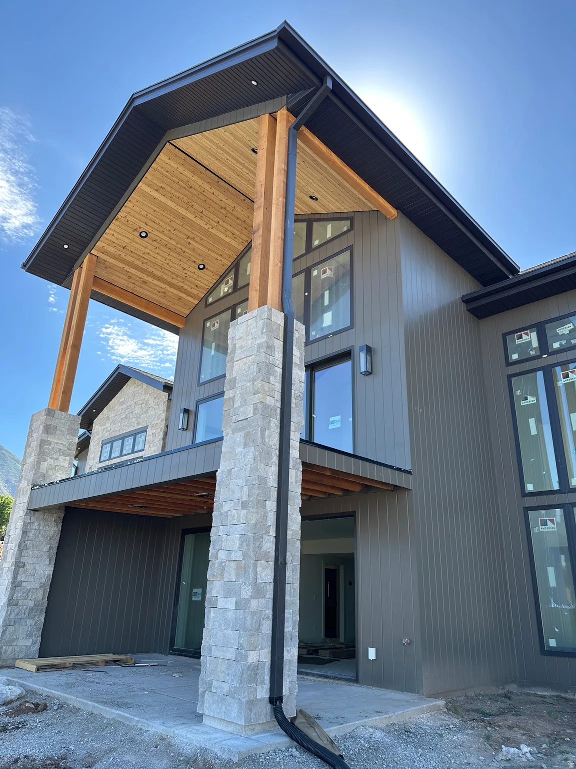 Modern exterior featuring multi-story stone columns, warm wood-finish soffits, and dark vertical siding