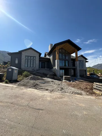 Modern architectural design featuring stone and dark siding, extensive fenestration, and a prominent covered entryway with exposed wood beams