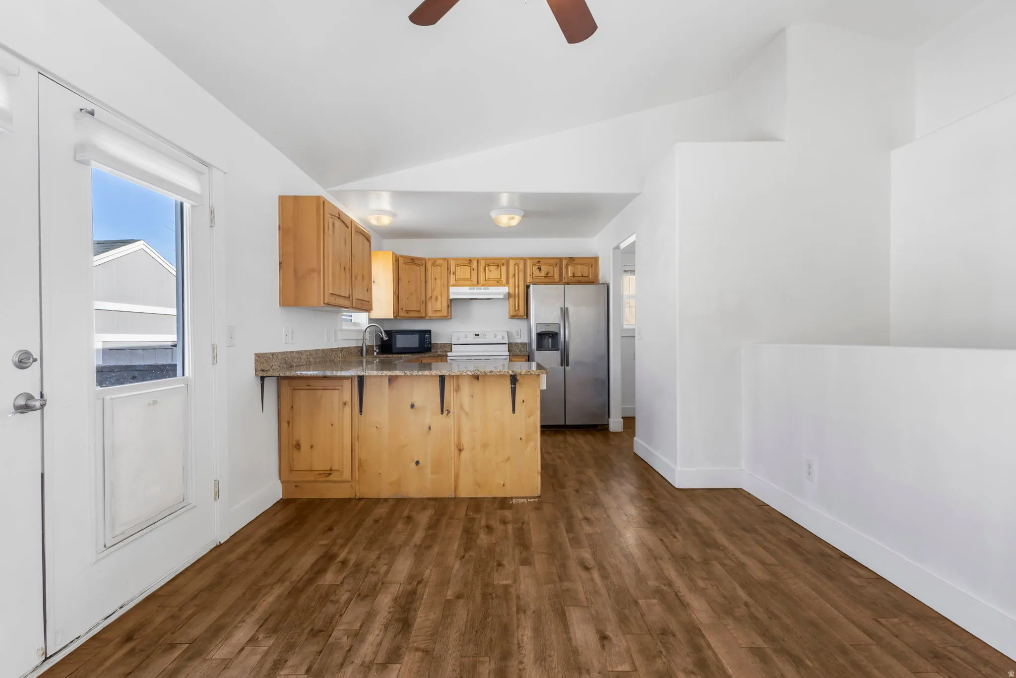 Kitchen with stainless steel refrigerator with ice dispenser, a peninsula, dark wood-style flooring, light stone countertops, and healthy amount of natural light