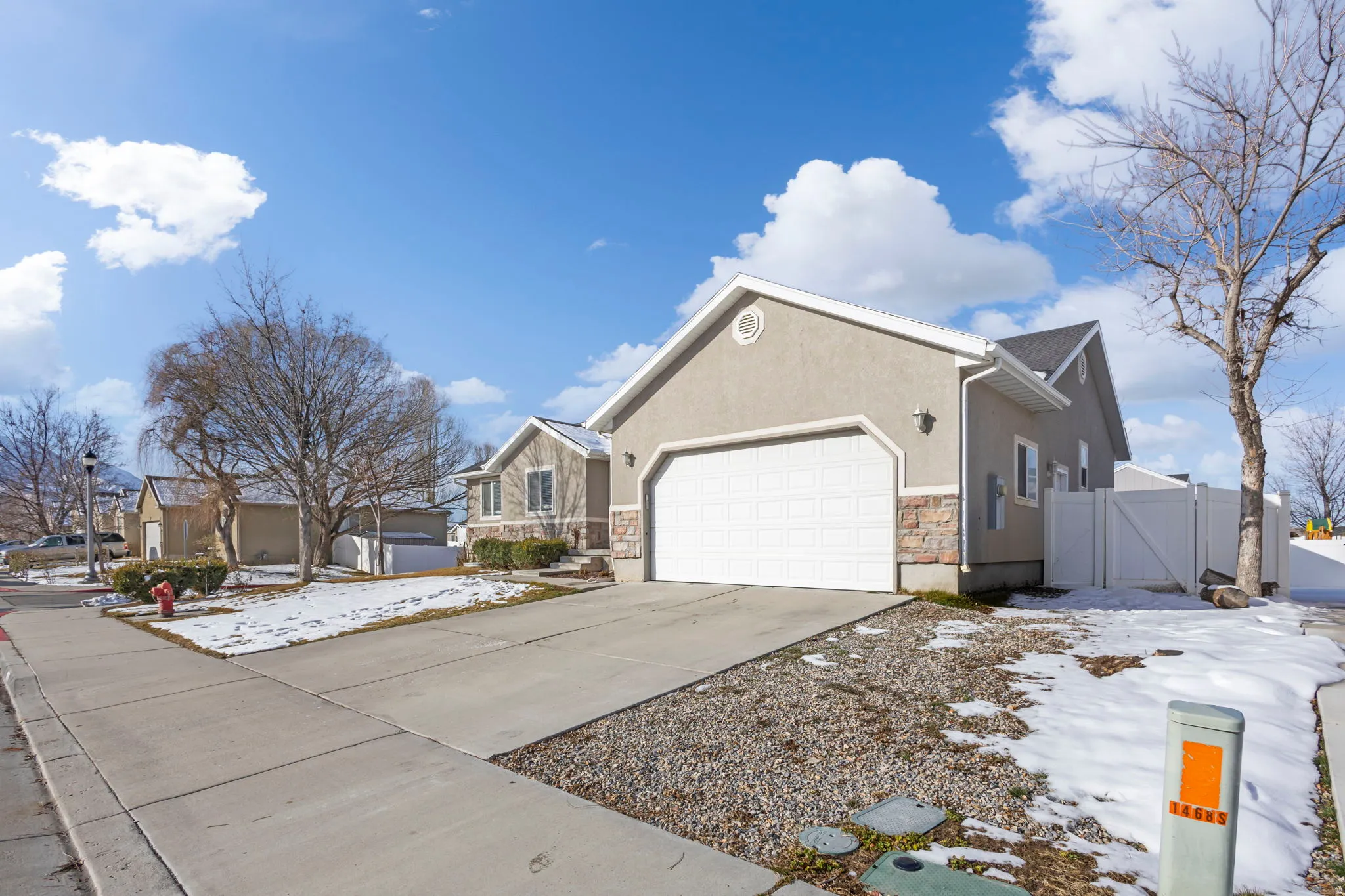 View of snowy exterior with stone siding, a gate, a garage, stucco siding, and concrete driveway
