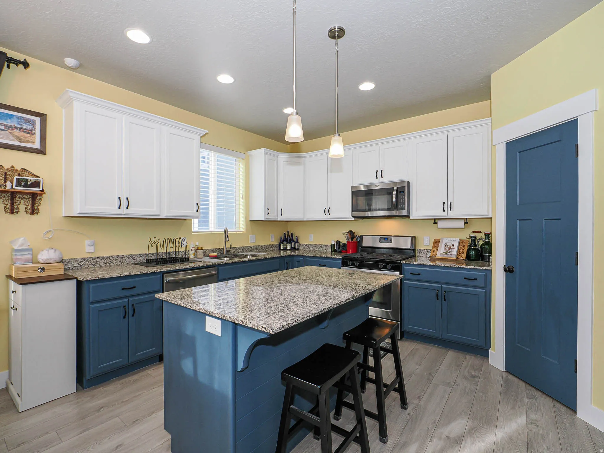 Kitchen featuring dual tone cabinetry, decorative light fixtures, light stone counters, stainless steel appliances, and a breakfast bar area