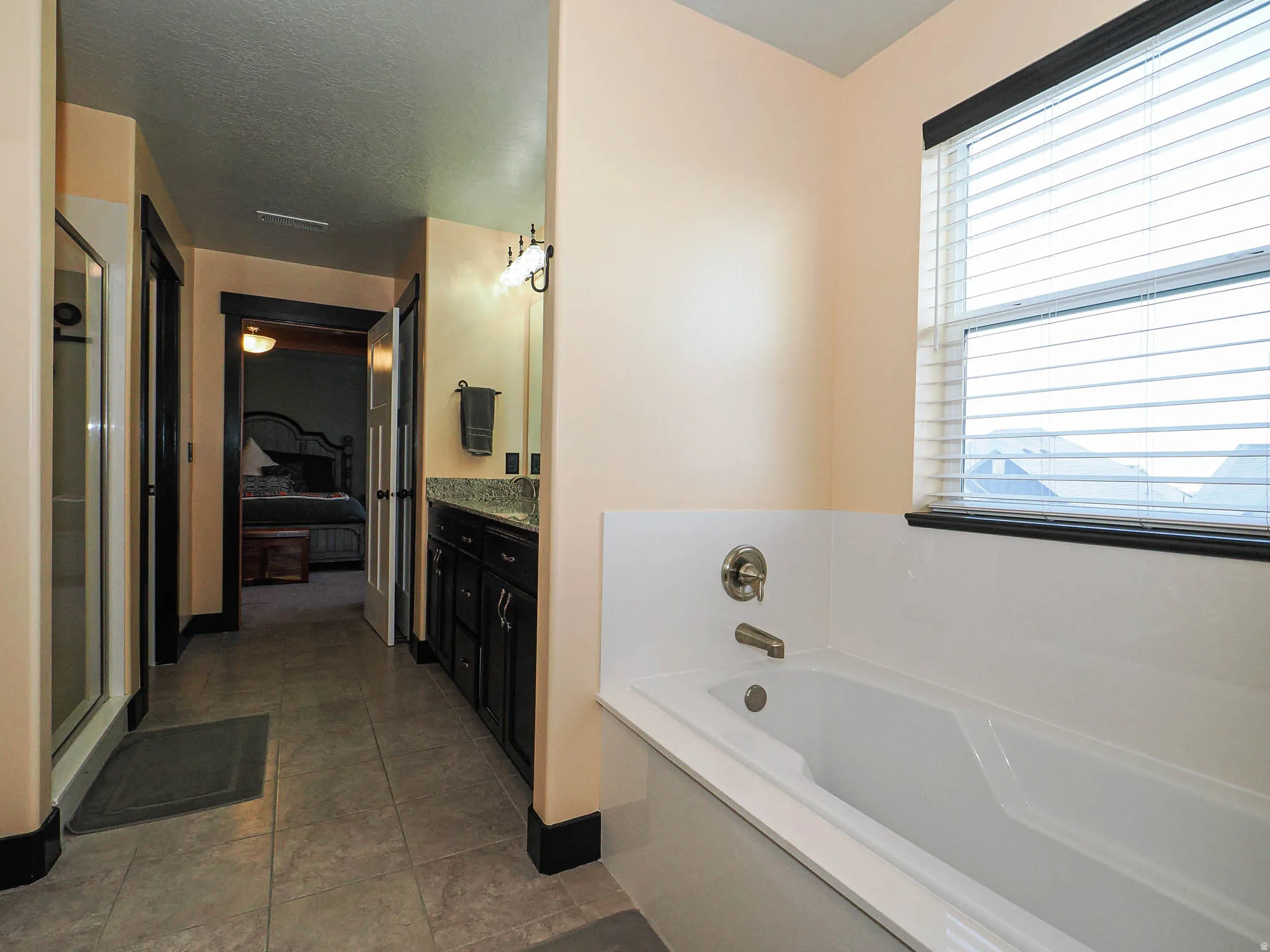 Ensuite bathroom featuring vanity, a bath, a stall shower, and dark tile patterned floors