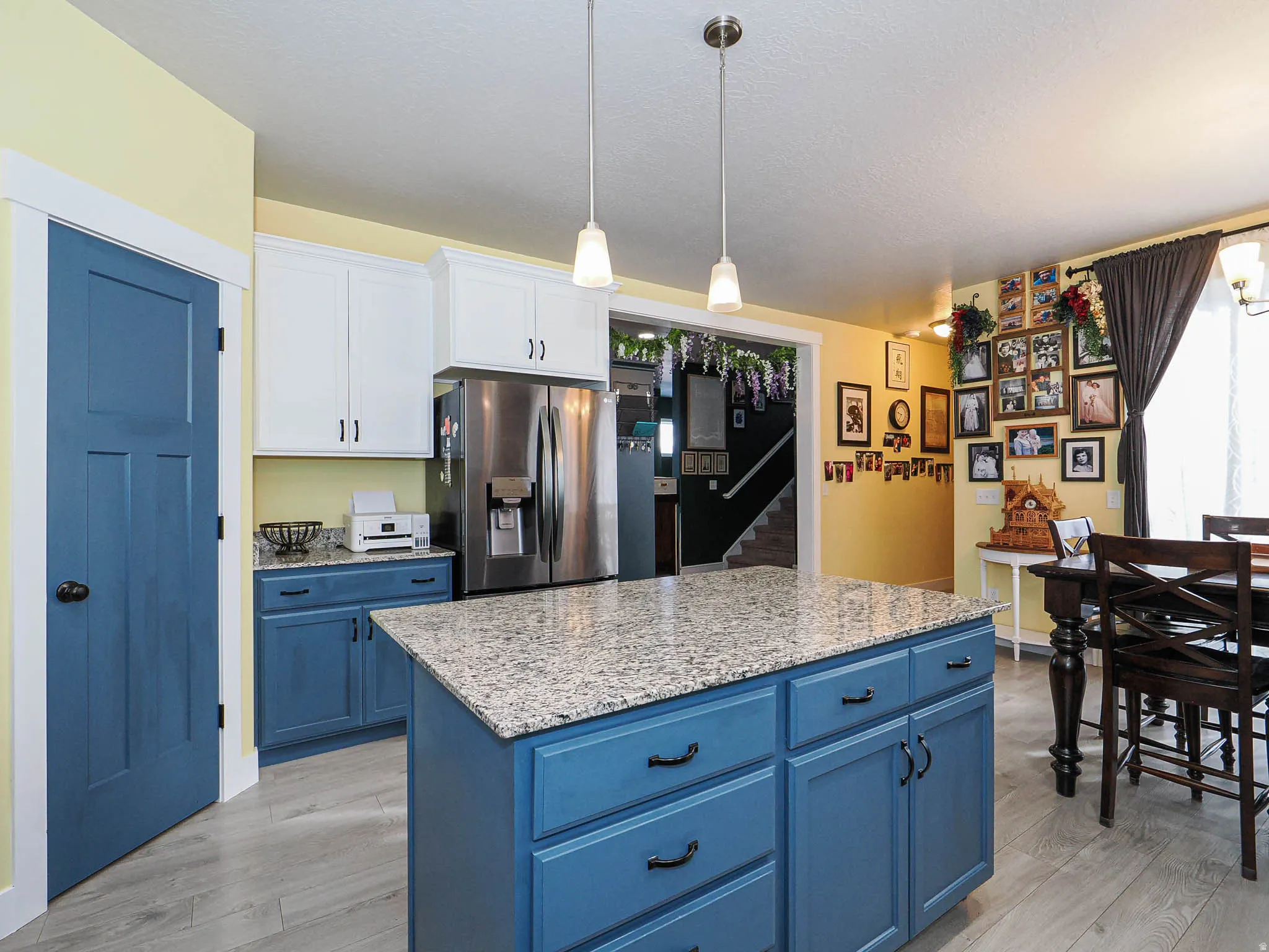 Dual tone kitchen with two tone cabinets, light stone counters, stainless steel fridge, hanging light fixtures, and a kitchen island