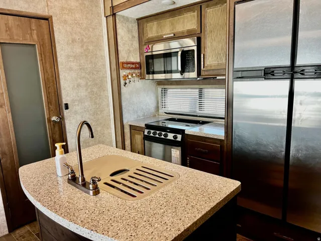 Kitchen featuring stainless steel appliances, an island with sink, and light stone countertops