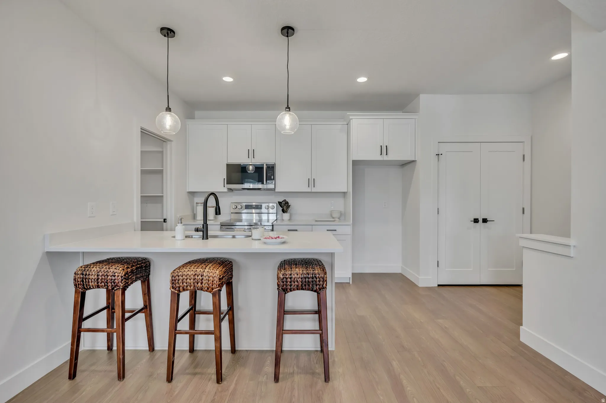 Kitchen with a kitchen bar, a peninsula, white cabinetry, stainless steel appliances, and hanging light fixtures