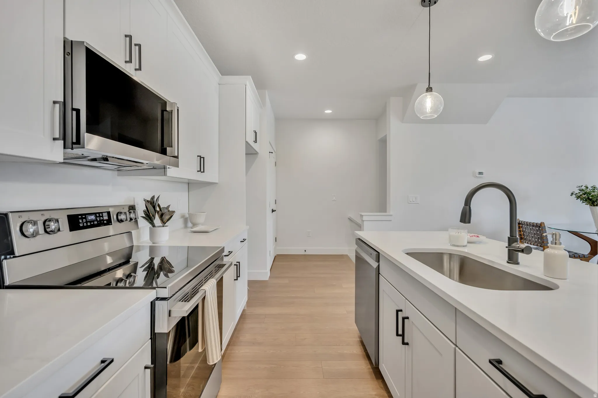 Kitchen with stainless steel appliances, white cabinets, light wood-type flooring, decorative light fixtures, and light stone countertops