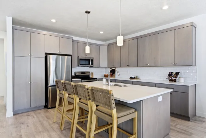 Kitchen with stainless steel appliances, gray cabinetry, a kitchen bar, and hanging light fixtures