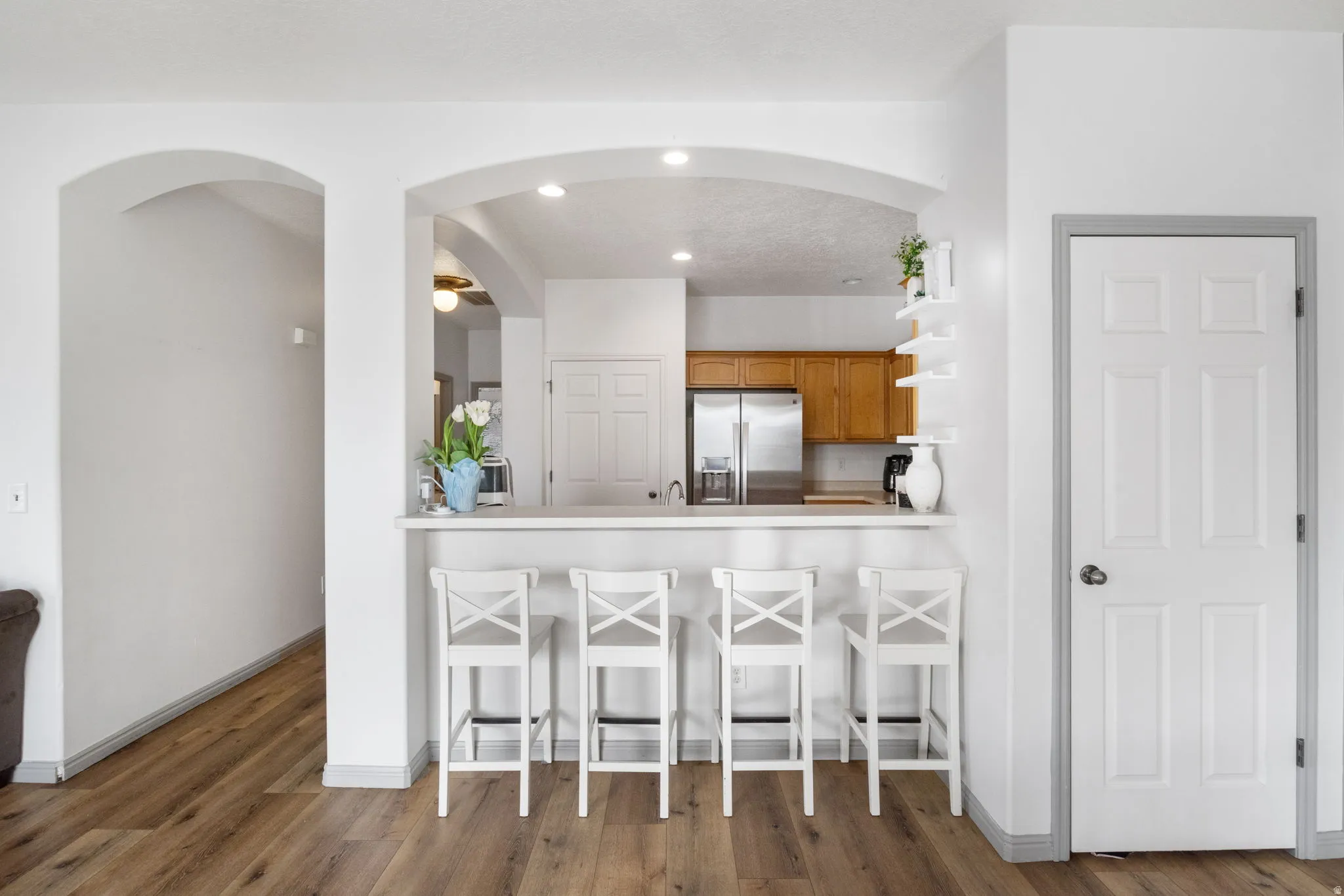 Kitchen featuring a breakfast bar area, light countertops, arched walkways, stainless steel fridge with ice dispenser, and dark wood-style floors