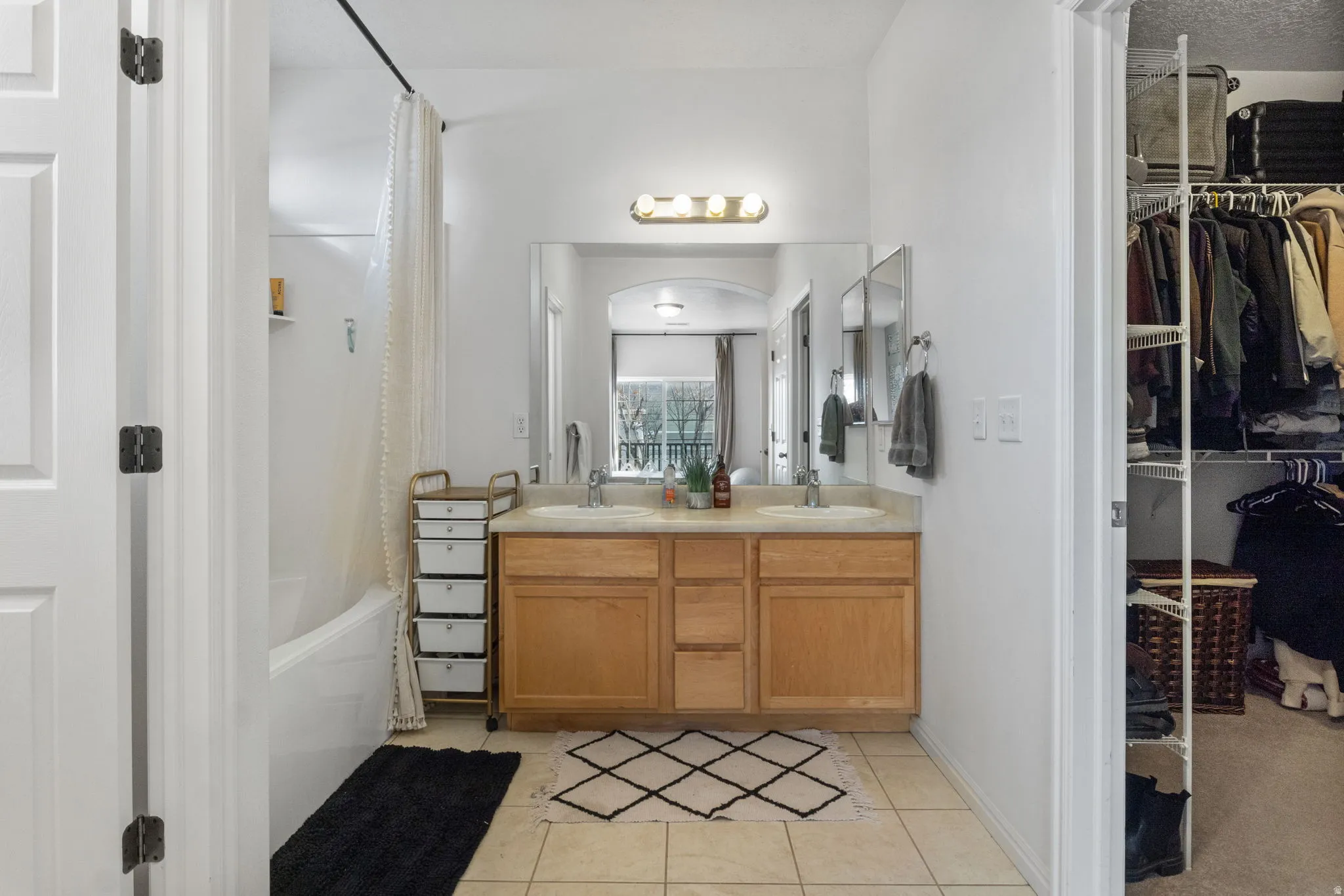 Ensuite bathroom featuring a spacious closet, double vanity, shower / bath combo, and light tile patterned floors