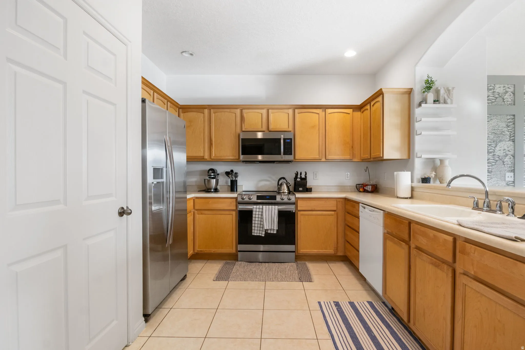Kitchen with stainless steel appliances, light countertops, light tile patterned flooring, and wood finish cabinets