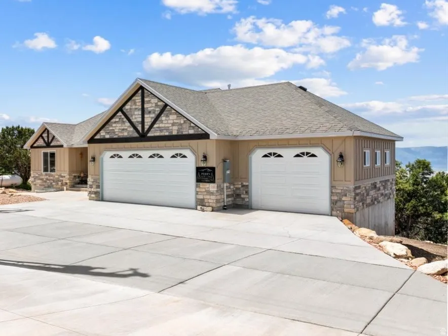 View of front of property featuring stone siding, a garage, concrete driveway, and a shingled roof