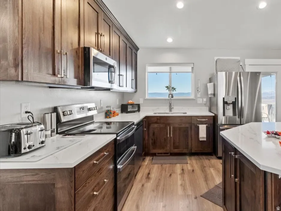 Kitchen featuring dark wood finish cabinets, stainless steel appliances, a kitchen breakfast bar, french doors, and light wood finished floors
