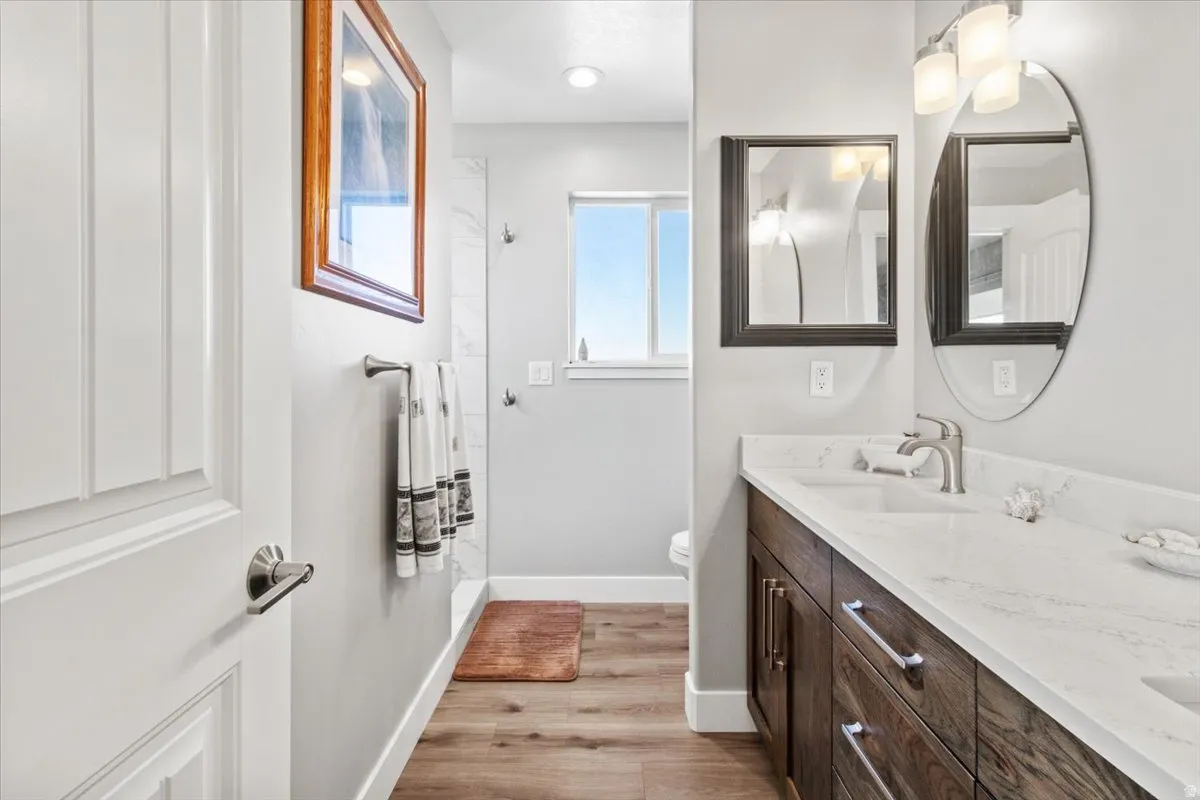 Bathroom with double vanity, a shower, and light wood-type flooring