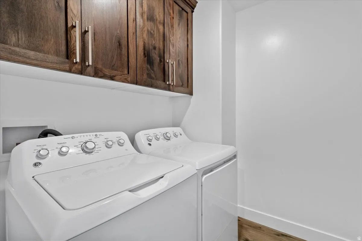 Laundry area with washer and dryer, cabinet space, and wood finished floors