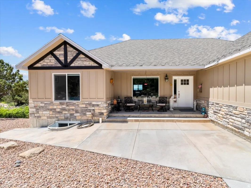 Property entrance featuring stone siding, board and batten siding, a shingled roof, and a patio area