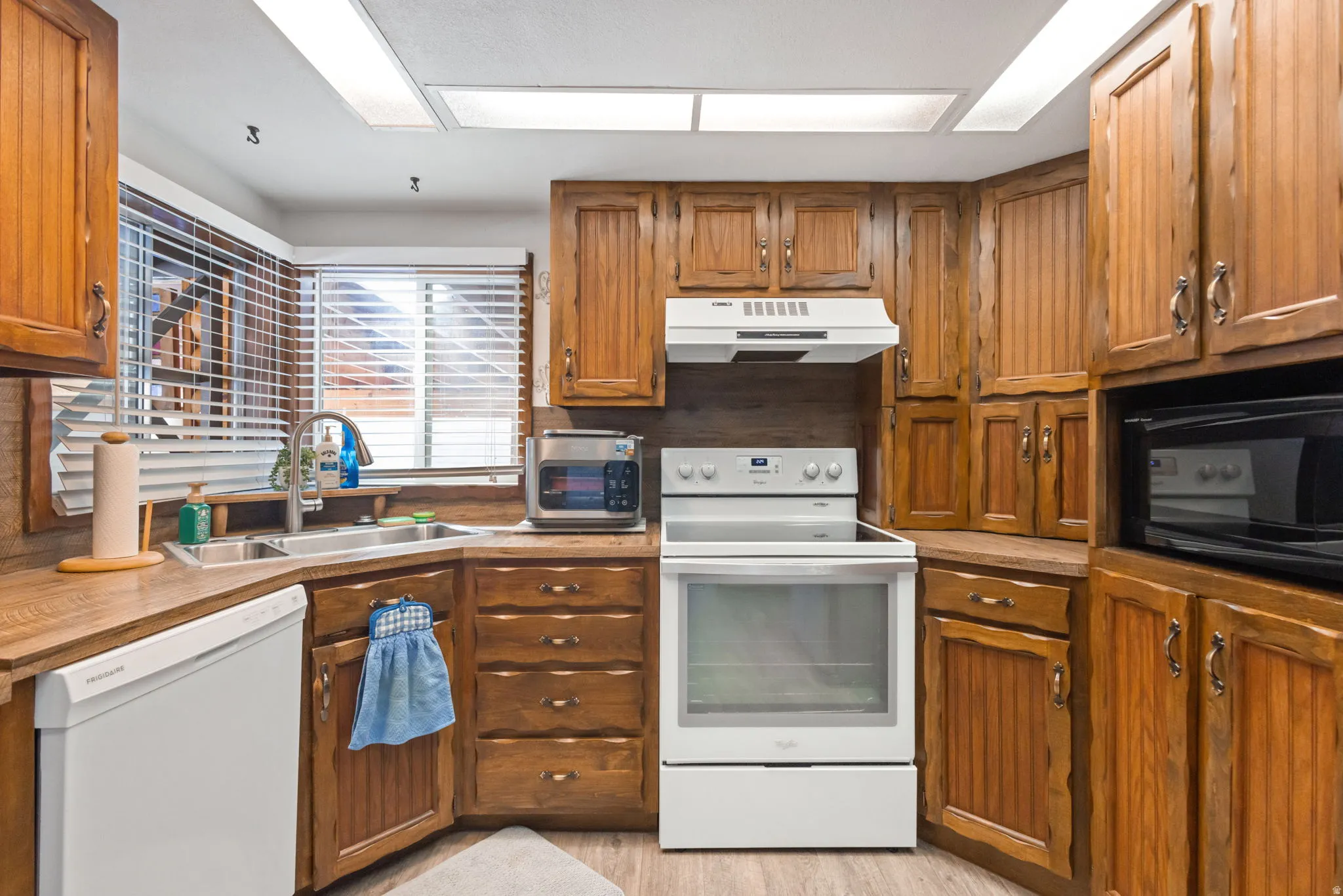Kitchen featuring white appliances, wood finish cabinets, light countertops, and light wood-style flooring