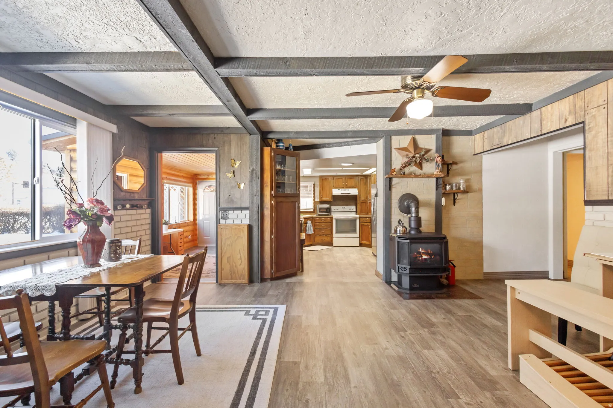 Dining area featuring light wood-type flooring, a wood stove, a ceiling fan, wooden walls, and a textured ceiling
