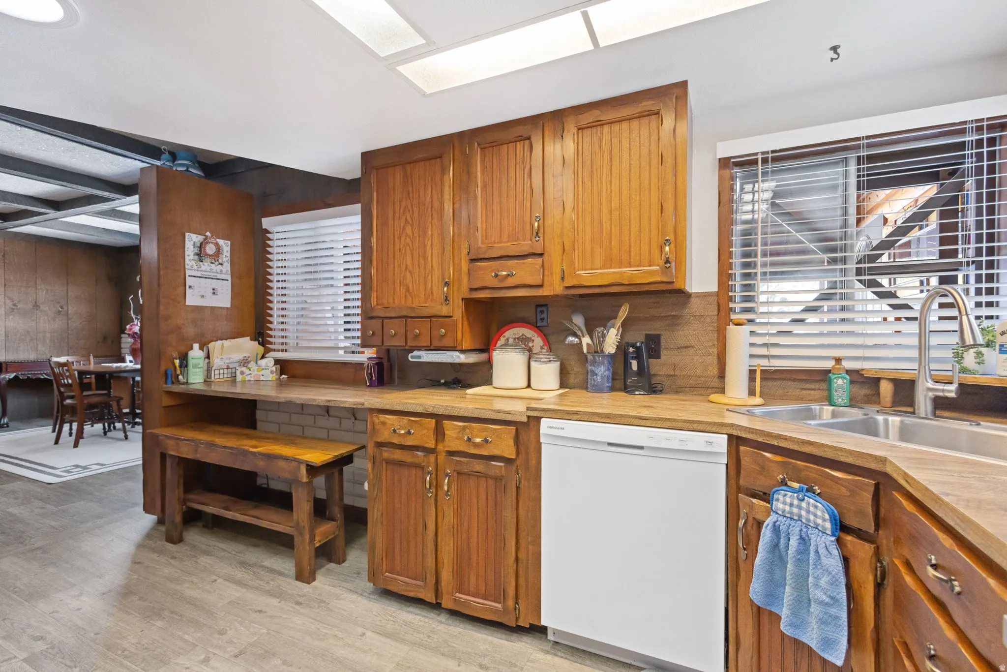 Kitchen with white dishwasher, wood finish cabinets, light countertops, and wood walls