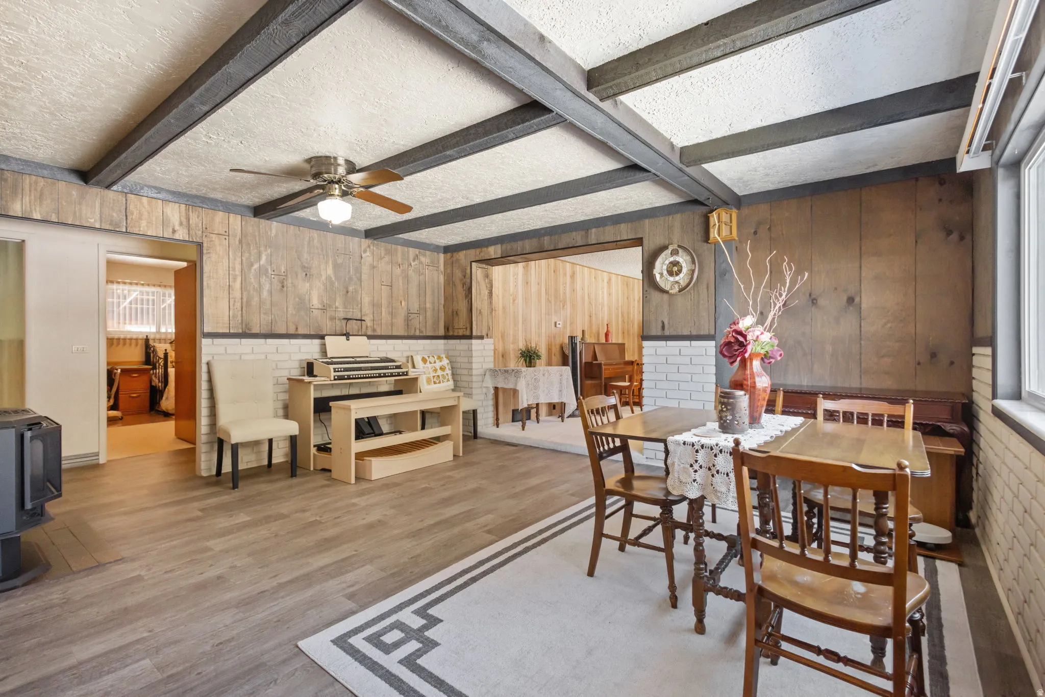Dining space with beam ceiling, wood finished floors, wood walls, a textured ceiling, and a ceiling fan