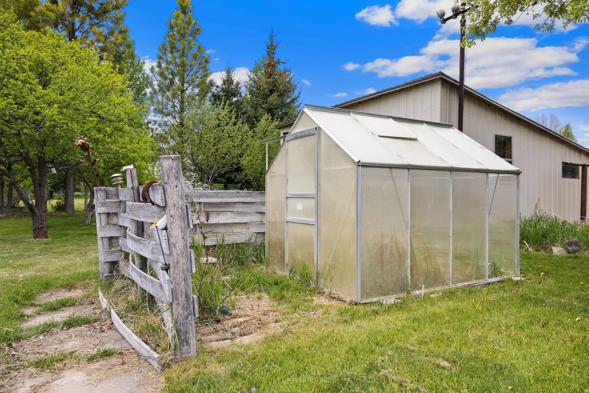 Standalone greenhouse structure featuring translucent paneling and a pitched roof design, set on a grassy expanse