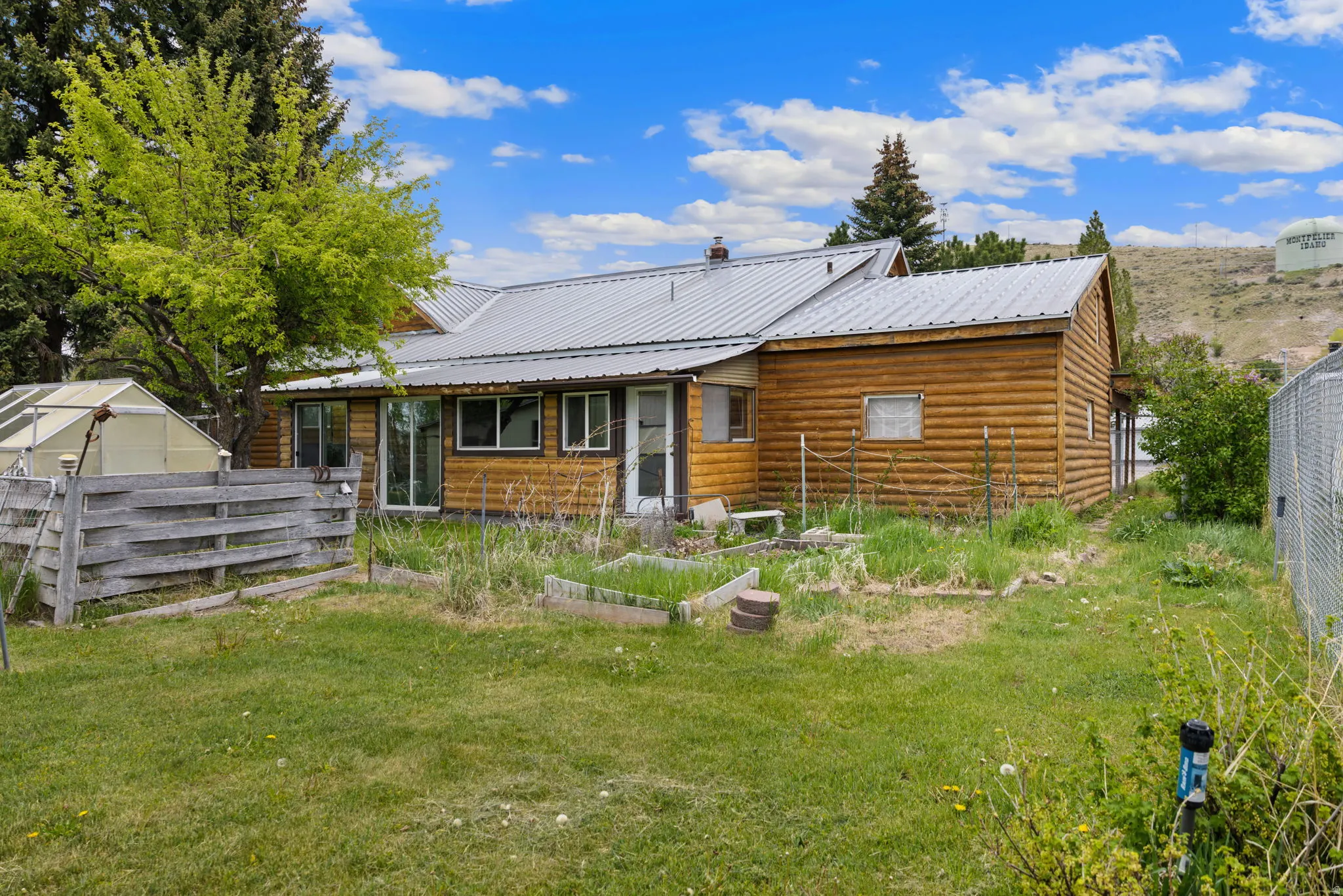Log exterior featuring a metal roof, multiple windows, a sliding glass door, and an attached greenhouse