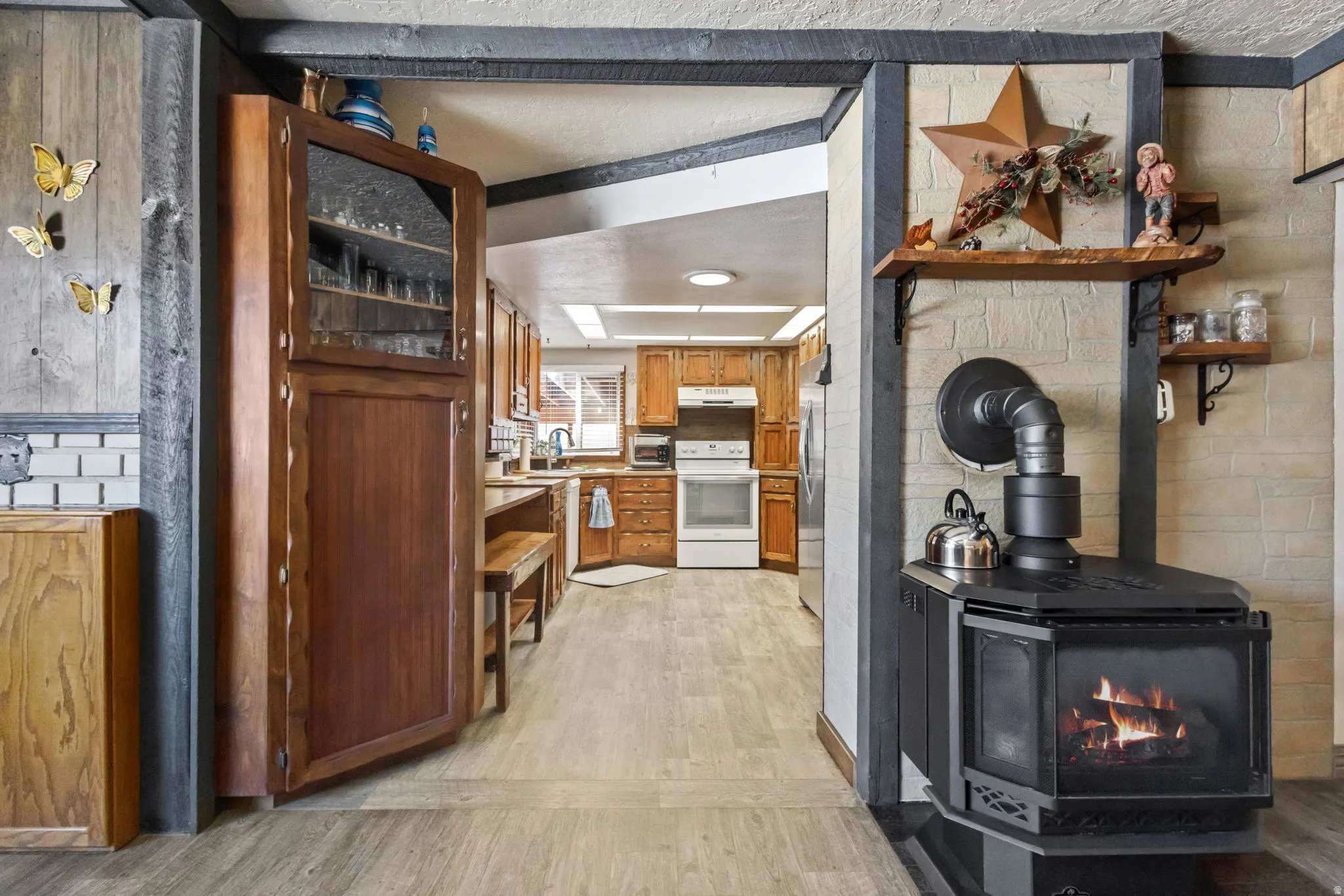 Kitchen featuring wood finish cabinets, open shelves, electric range, a wood stove, and light wood-style floors