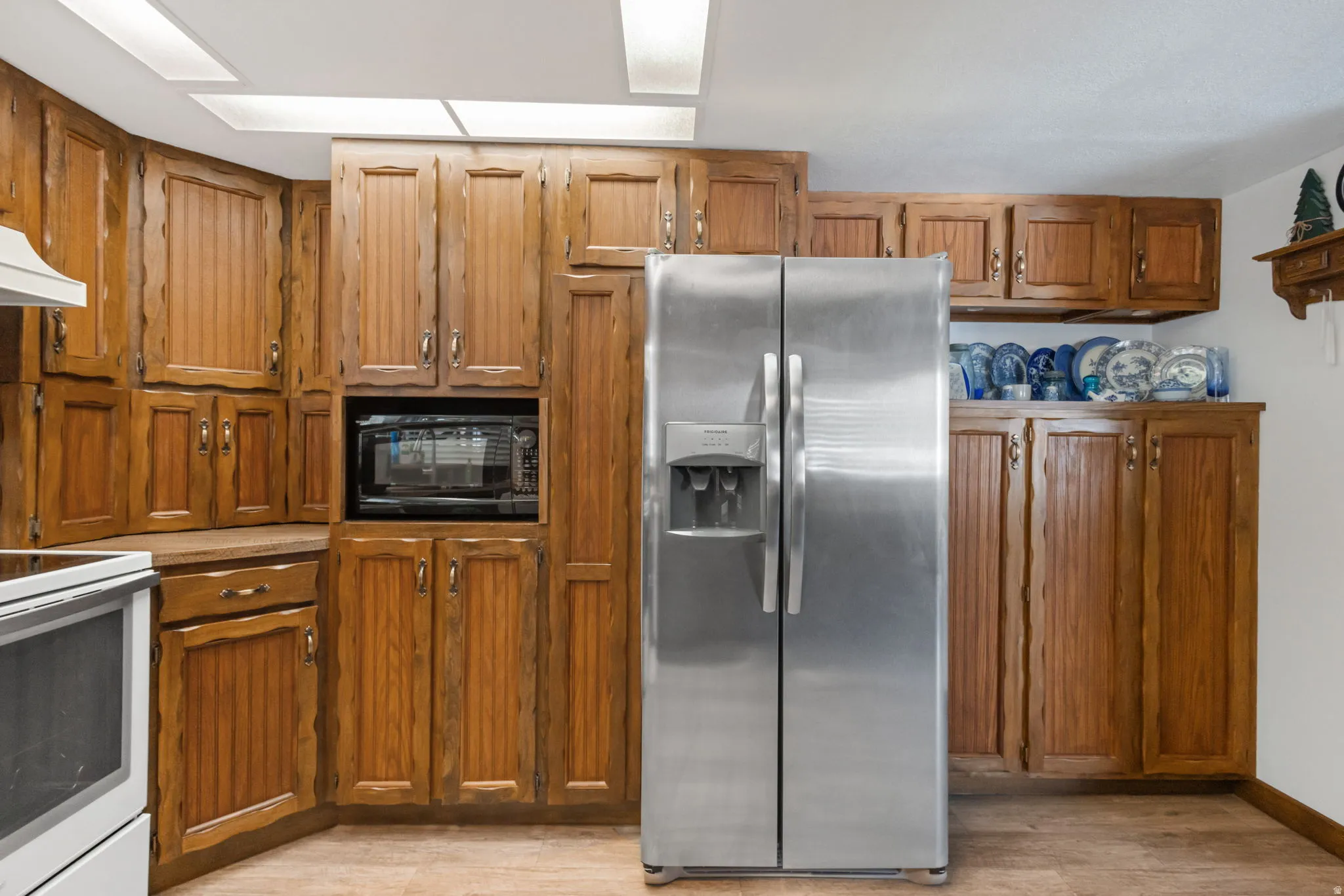 Kitchen featuring stainless steel fridge with ice dispenser, wood finish cabinetry, white range with electric cooktop, and black microwave