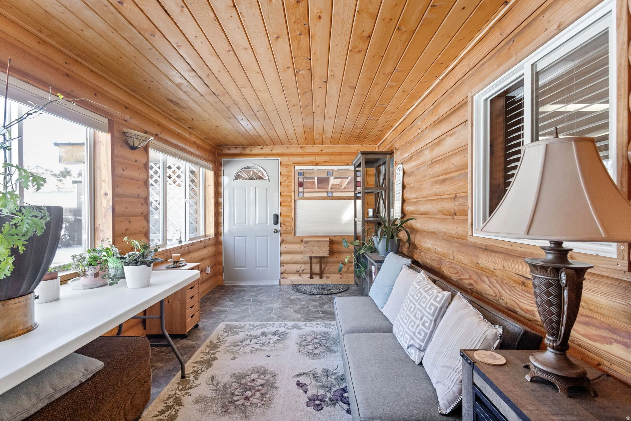 Sunroom featuring natural wood paneling, wood-plank ceiling, multiple windows, a white entry door with an arched window insert, and slate-style flooring