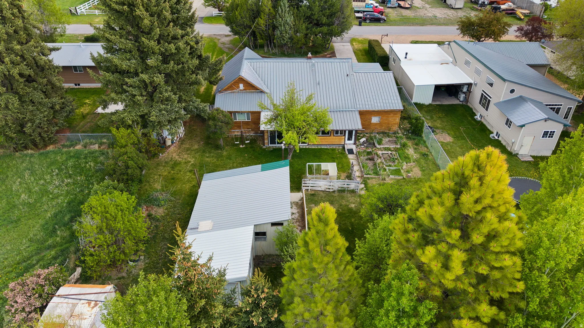Aerial perspective showcasing multiple structures with metal roofing, extensive landscaping, and a fenced yard
