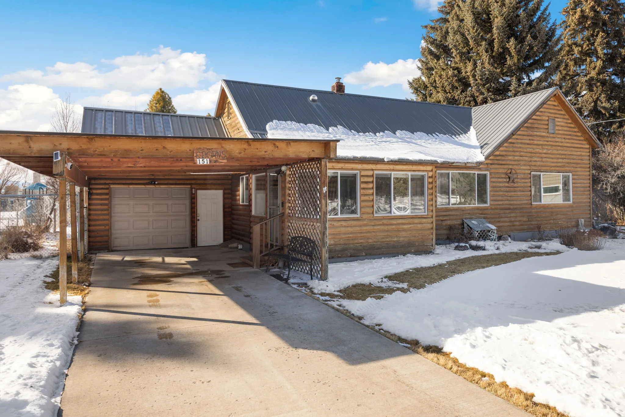 Rustic home with a metal roof, concrete driveway, a chimney, a carport, and log veneer siding
