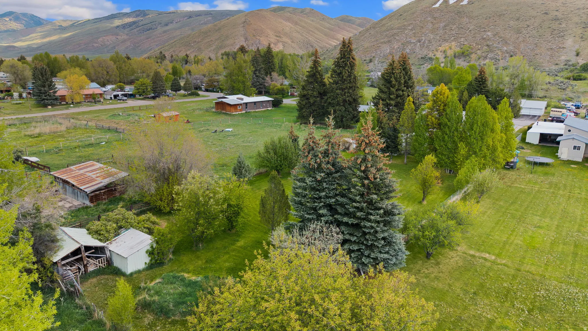 Expansive property featuring verdant lawns, mature evergreen trees, various outbuildings, and distant mountain backdrops