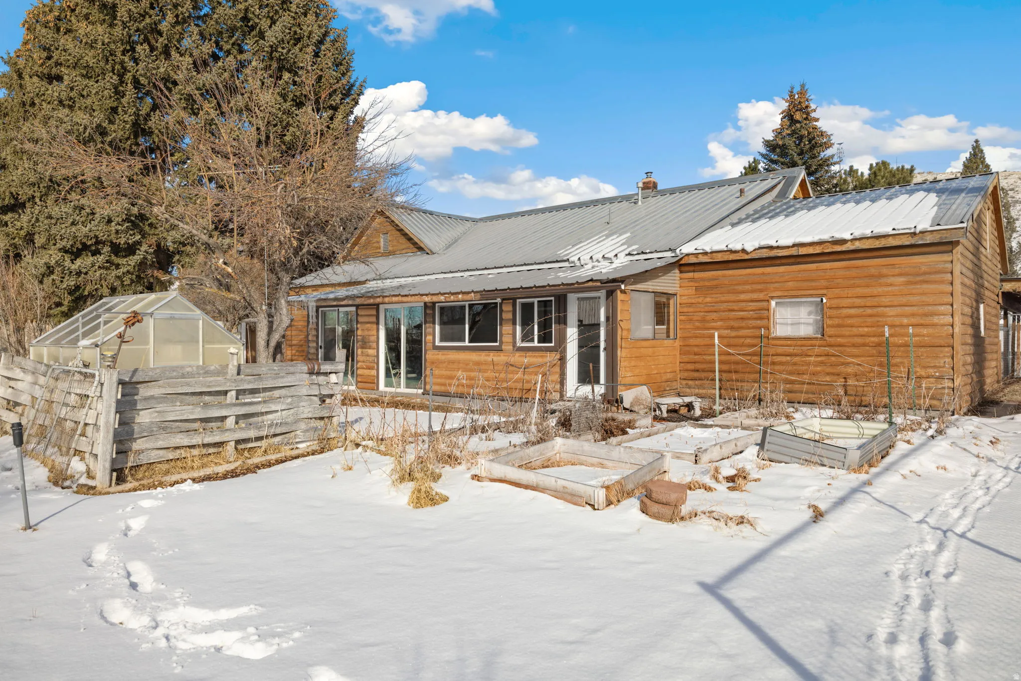 Snow covered rear of property with a vegetable garden, an exterior structure, an outbuilding, and a metal roof