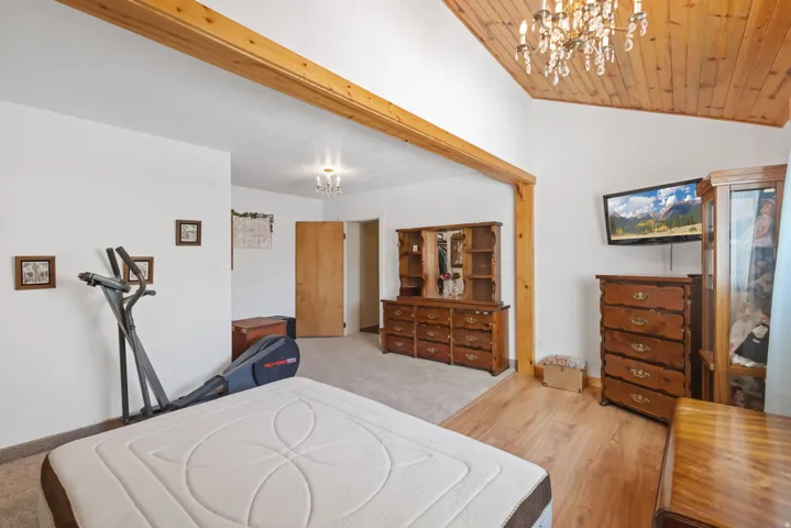 Bedroom featuring hanging lights, light wood finished floors, and a vaulted wooden ceiling