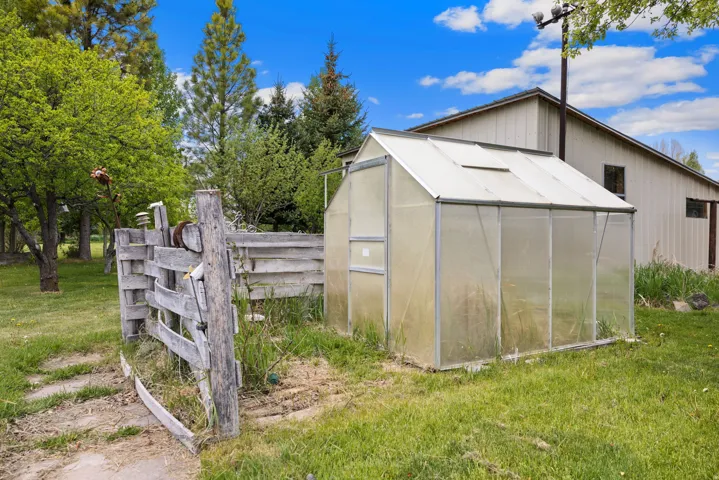 Standalone greenhouse structure featuring translucent paneling and a pitched roof design, set on a grassy expanse