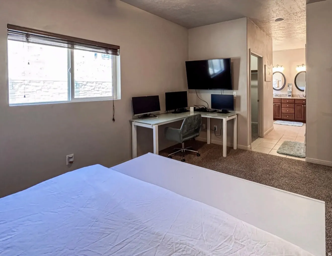 Bedroom with connected bathroom, a desk, light carpet, and a textured ceiling