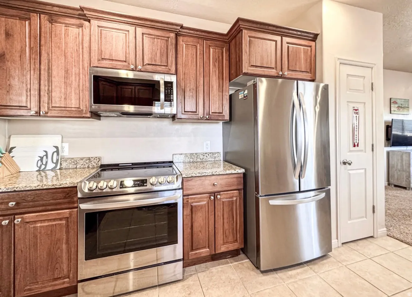 Kitchen featuring stainless steel appliances, light stone countertops, wood finish cabinets, and light tile patterned flooring