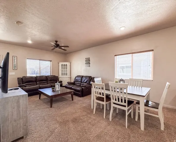 Living area with light carpet, a ceiling fan, a textured ceiling, and recessed lighting