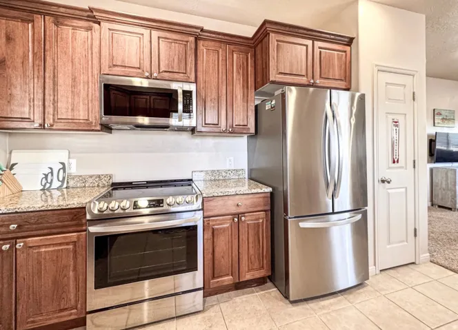 Kitchen featuring stainless steel appliances, light stone countertops, wood finish cabinets, and light tile patterned flooring